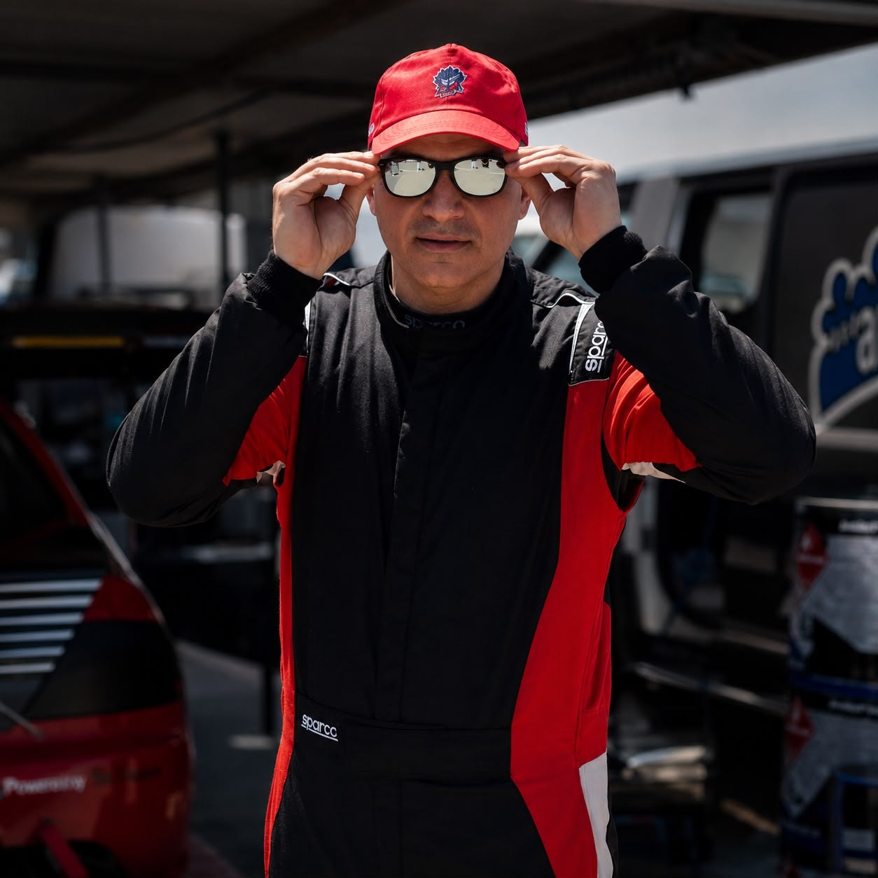 Michael Milonas at the track, adjusting his sunglasses, dressed in racing gear