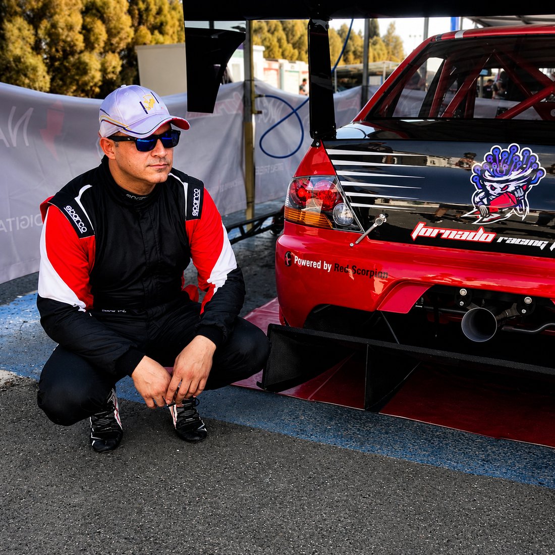 Michael Milonas crouched beside the Tornado Racing car in the pit lane